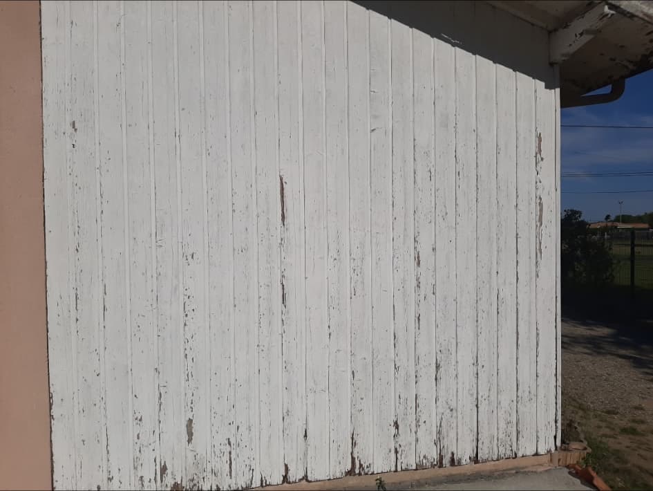 Lambris extérieur en bois avant remplacement, peinture blanche écaillée et lames abîmées en pied