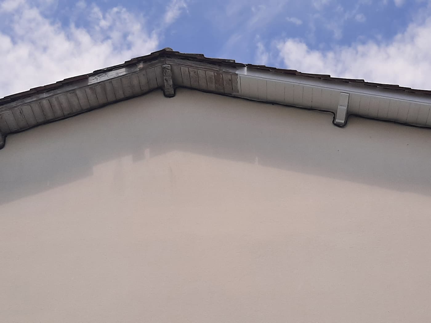 Débord de toit en cours de peinture, versant gauche encore grisé et versant droit repeint
